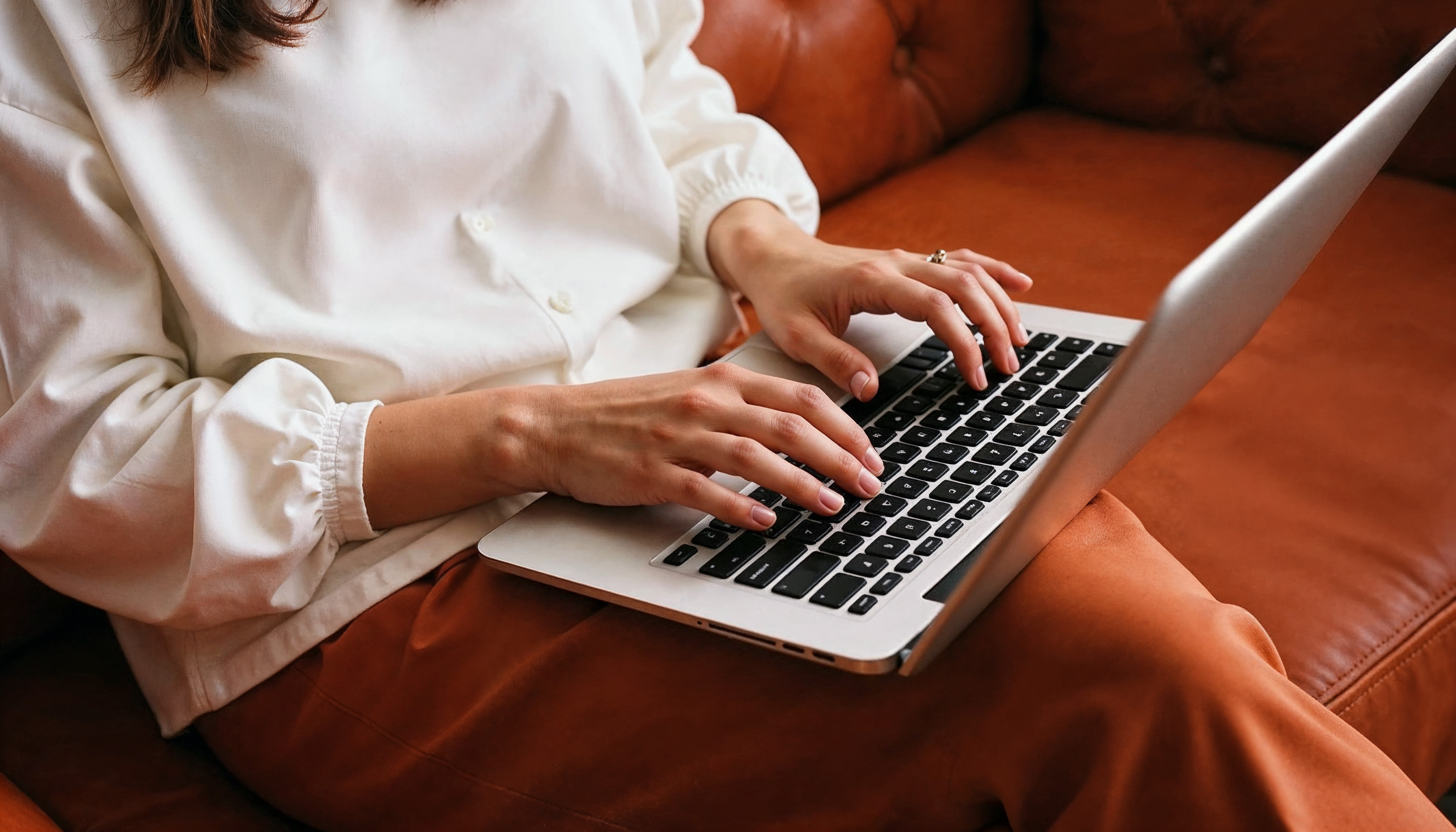 Dłonie nad klawiaturą laptopa, obok notes z zapisaną datą wyjazdu